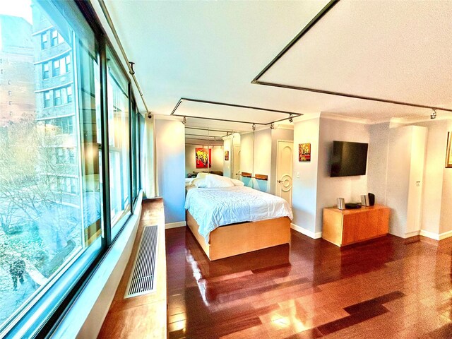 bedroom with visible vents, baseboards, wood finished floors, and track lighting