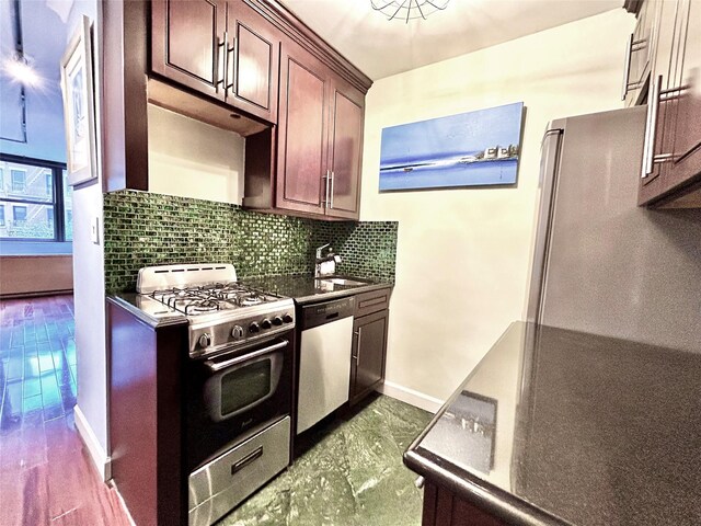 kitchen featuring tasteful backsplash, dark countertops, baseboards, stainless steel appliances, and a sink