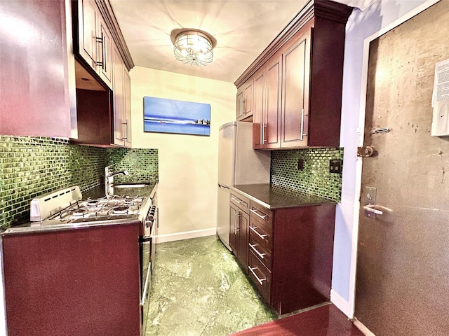 kitchen with a sink, dark countertops, freestanding refrigerator, gas stove, and baseboards