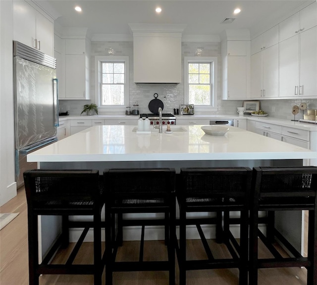 kitchen with visible vents, light countertops, ornamental molding, backsplash, and an island with sink