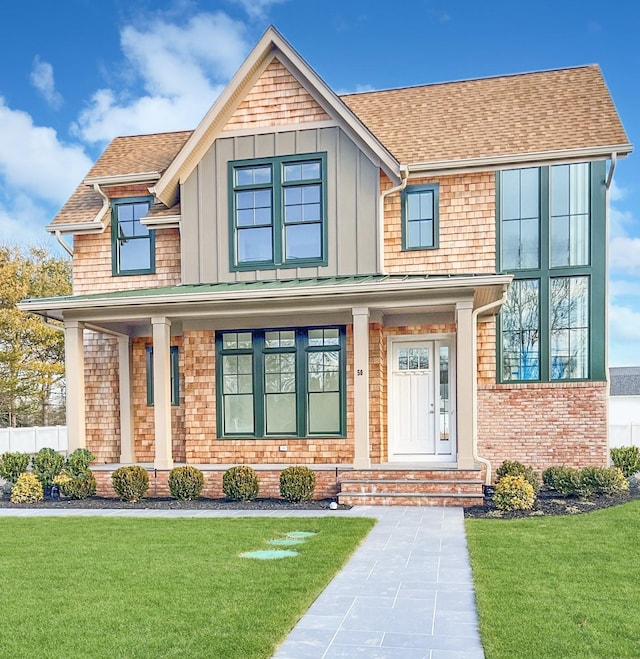 view of front of house with board and batten siding, brick siding, a shingled roof, and a front lawn