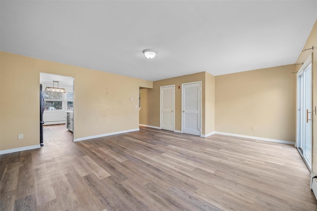 interior space featuring multiple closets, light wood-style floors, freestanding refrigerator, a baseboard heating unit, and baseboards