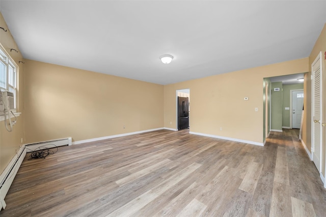 spare room with a baseboard heating unit, light wood-style flooring, and baseboards