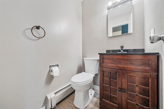 half bath featuring a baseboard radiator, toilet, vanity, wood finished floors, and baseboards