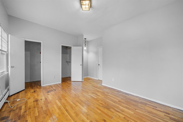 unfurnished bedroom featuring a walk in closet, a closet, baseboards, and light wood finished floors