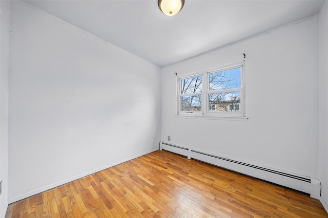 empty room with a baseboard heating unit, baseboards, and light wood-style floors