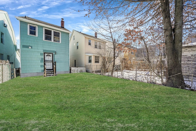 back of house with entry steps, a chimney, fence, and a lawn