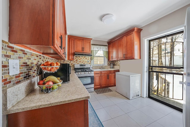 kitchen with light tile patterned floors, gas range, refrigerator, a sink, and backsplash