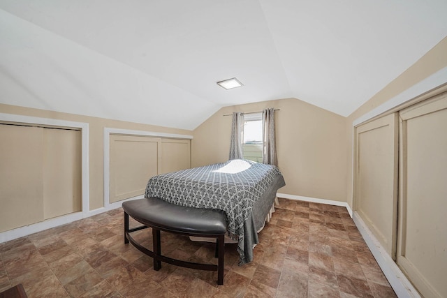 bedroom featuring lofted ceiling, baseboards, and multiple closets