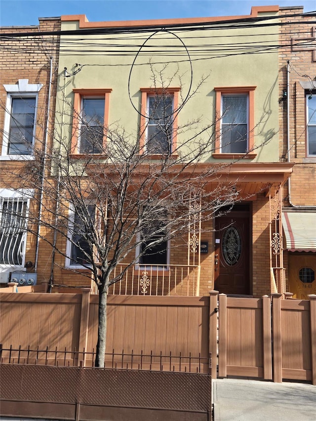 multi unit property with stucco siding, a fenced front yard, a gate, and brick siding