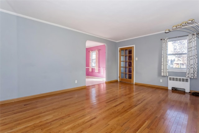 spare room featuring arched walkways, crown molding, radiator, light wood-style floors, and baseboards