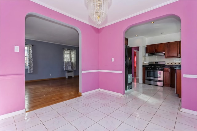 kitchen with arched walkways, under cabinet range hood, black fridge, radiator, and stainless steel range with gas stovetop