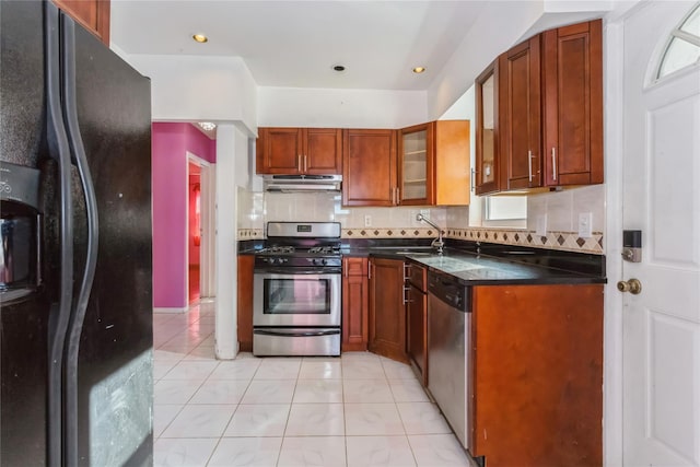 kitchen with light tile patterned floors, under cabinet range hood, stainless steel appliances, a sink, and decorative backsplash