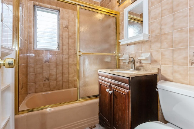 full bathroom featuring toilet, bath / shower combo with glass door, vanity, and tile walls