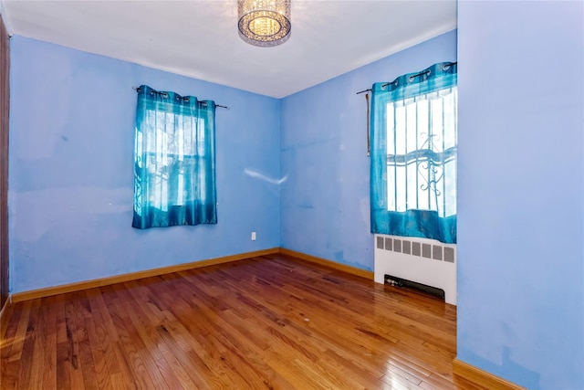 empty room with radiator, hardwood / wood-style flooring, baseboards, and a chandelier