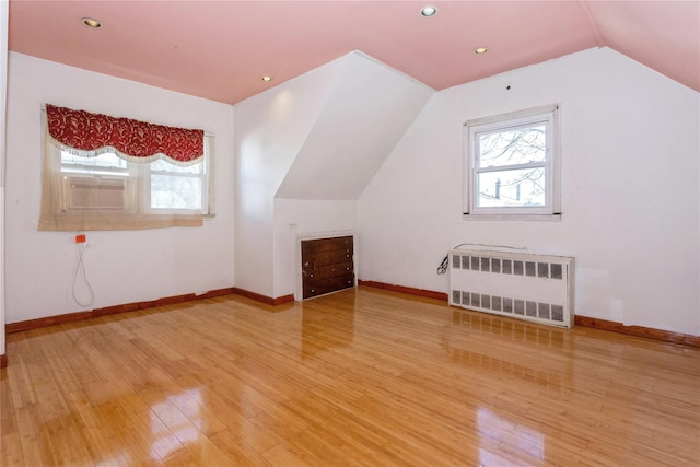 bonus room with cooling unit, light wood-style flooring, baseboards, vaulted ceiling, and radiator heating unit