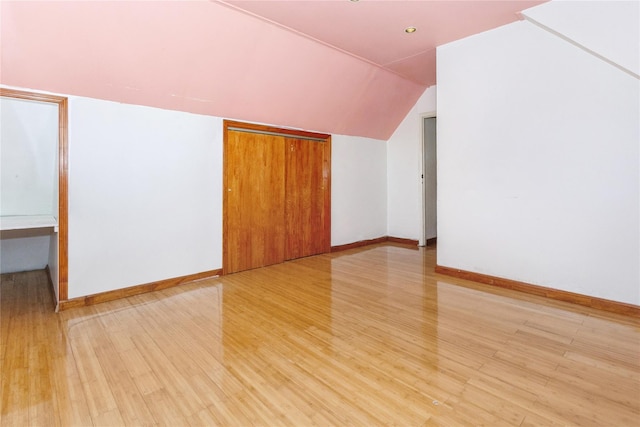 additional living space with light wood-style floors, baseboards, and vaulted ceiling