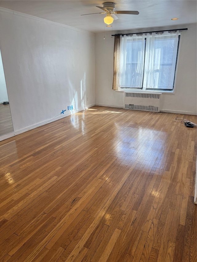 unfurnished room with ceiling fan, baseboards, ornamental molding, radiator heating unit, and wood-type flooring