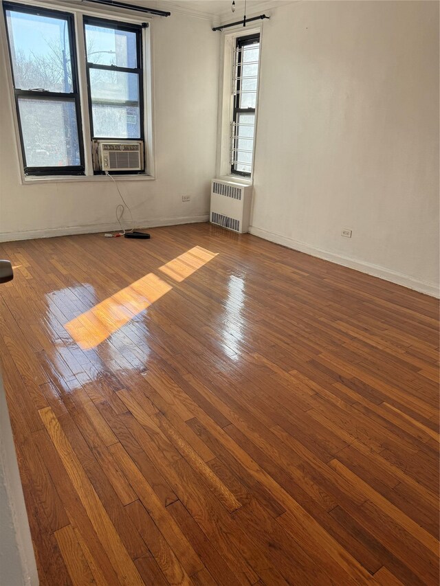 empty room featuring radiator heating unit, cooling unit, hardwood / wood-style flooring, and baseboards