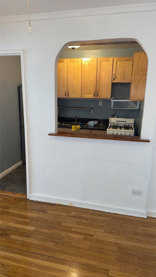 kitchen featuring dark wood-style flooring, gas range gas stove, dark countertops, ornamental molding, and baseboards