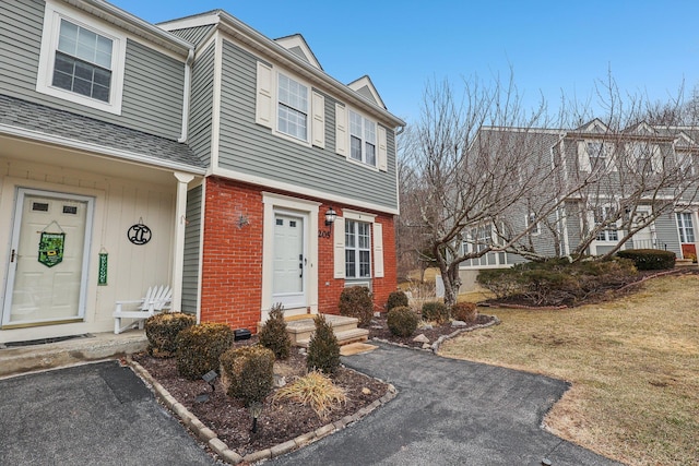 townhome / multi-family property with brick siding, a front lawn, and roof with shingles