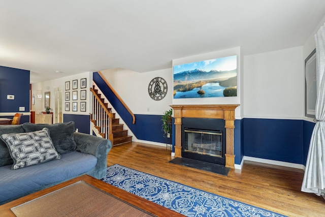 living area with a fireplace with flush hearth, stairs, baseboards, and wood finished floors