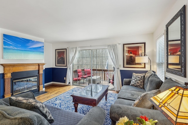 living area featuring a fireplace with flush hearth, baseboards, and wood finished floors