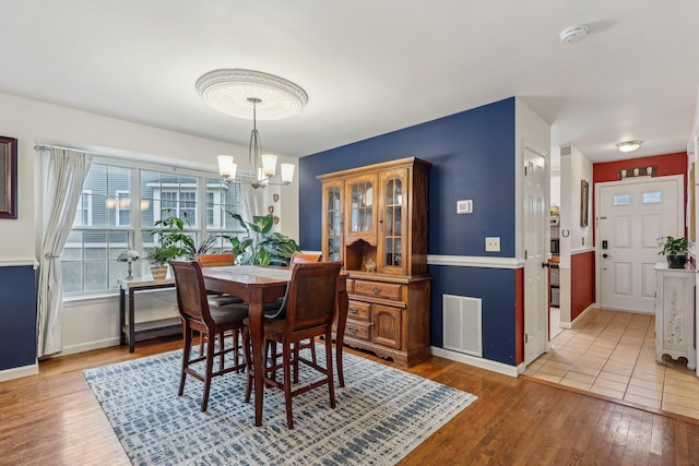 dining space with baseboards, visible vents, a notable chandelier, and wood finished floors