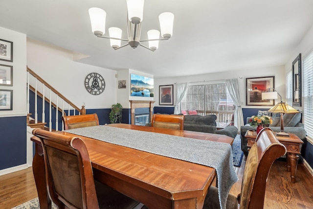 dining space featuring baseboards, a glass covered fireplace, wood finished floors, an inviting chandelier, and stairs