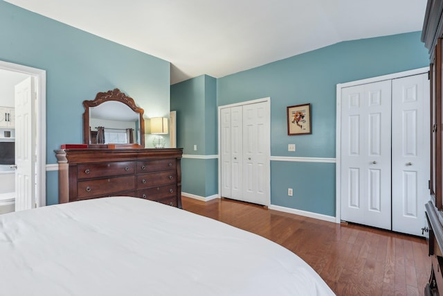 bedroom with baseboards, connected bathroom, wood finished floors, vaulted ceiling, and multiple closets