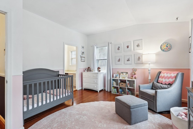 bedroom with vaulted ceiling, a crib, and wood finished floors