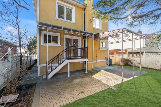 rear view of house featuring a yard, central AC unit, a fenced backyard, and stucco siding