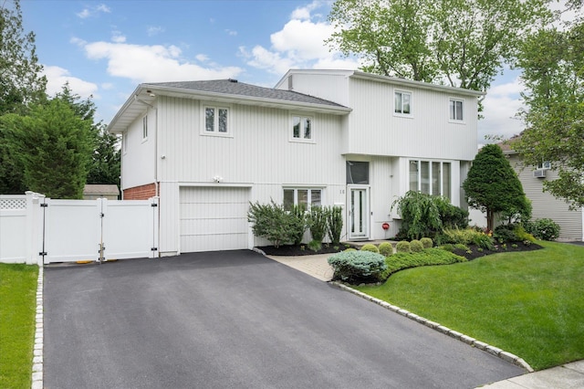 view of front facade with driveway, an attached garage, a gate, fence, and a front lawn