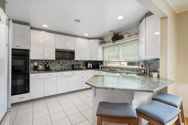 kitchen featuring light tile patterned floors, a peninsula, black appliances, white cabinetry, and a sink