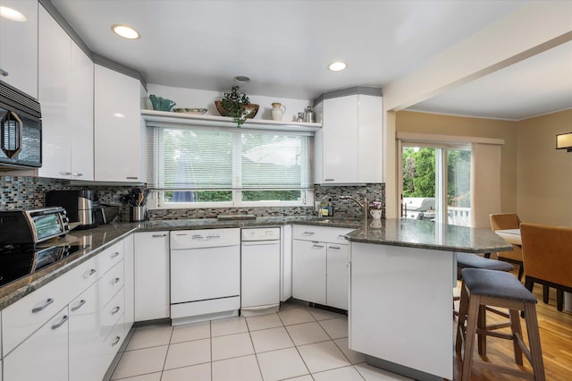 kitchen featuring black microwave, white dishwasher, a peninsula, a sink, and a kitchen breakfast bar