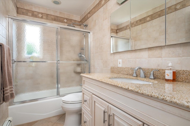 bathroom featuring tile patterned flooring, a baseboard heating unit, vanity, tile walls, and combined bath / shower with glass door