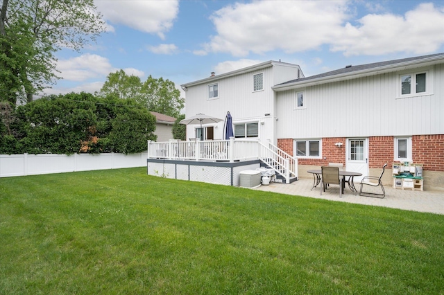 rear view of house featuring a deck, brick siding, a lawn, and fence