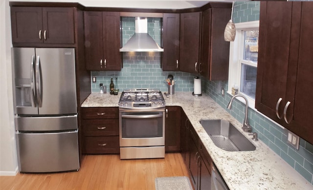 kitchen featuring wall chimney exhaust hood, appliances with stainless steel finishes, a sink, and light wood-style flooring