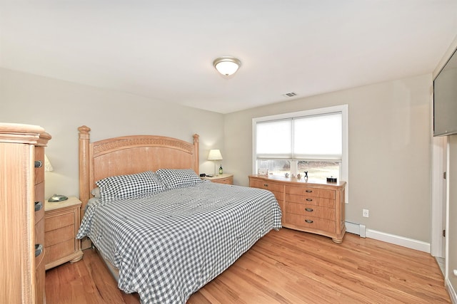 bedroom with light wood-style floors, visible vents, a baseboard heating unit, and baseboards