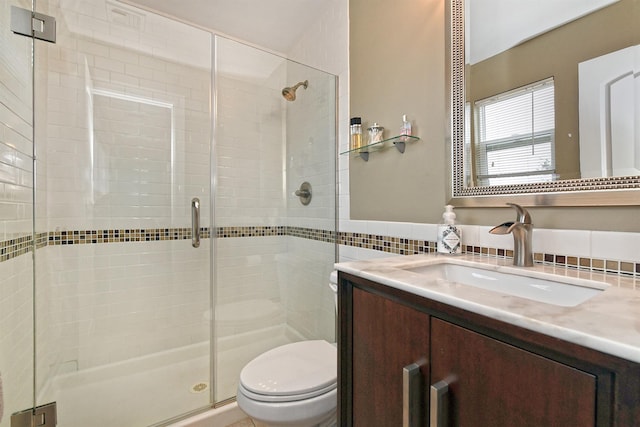 full bath featuring a stall shower, tile walls, toilet, and vanity