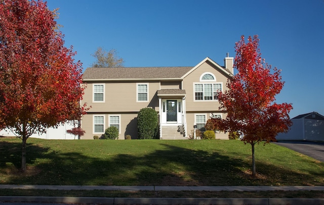 raised ranch with a shingled roof, a front yard, and a chimney