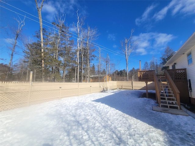 yard layered in snow featuring a fenced backyard, stairs, and a wooden deck