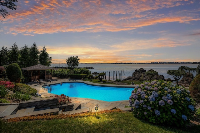 pool at dusk featuring an outdoor pool, a water view, a patio, and a gazebo