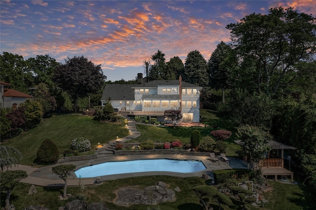 pool at dusk with a deck, a lawn, stairs, and an outdoor pool