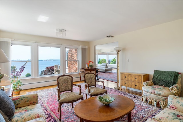 living area featuring a baseboard heating unit, visible vents, a water view, and wood finished floors