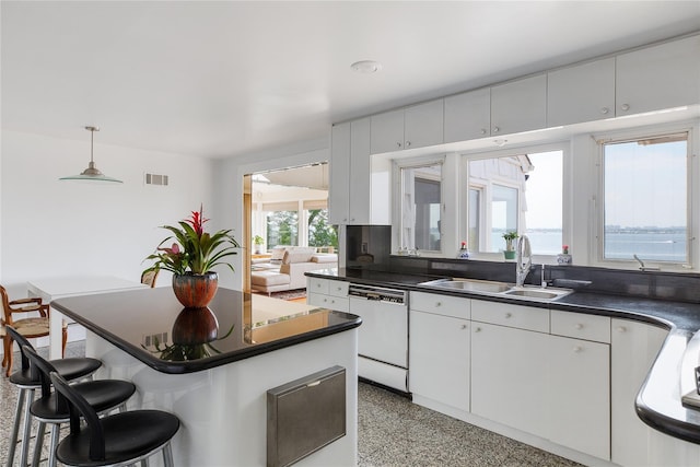 kitchen with dark countertops, visible vents, white dishwasher, a sink, and a kitchen breakfast bar