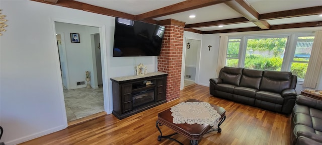 living room featuring beam ceiling, visible vents, light wood-style flooring, and baseboards