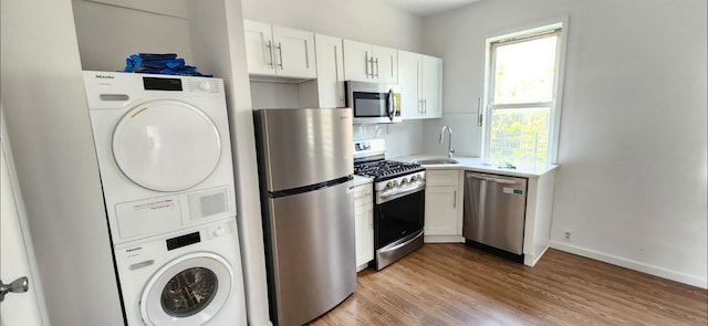 kitchen featuring stacked washer and clothes dryer, light countertops, stainless steel appliances, light wood-type flooring, and a sink