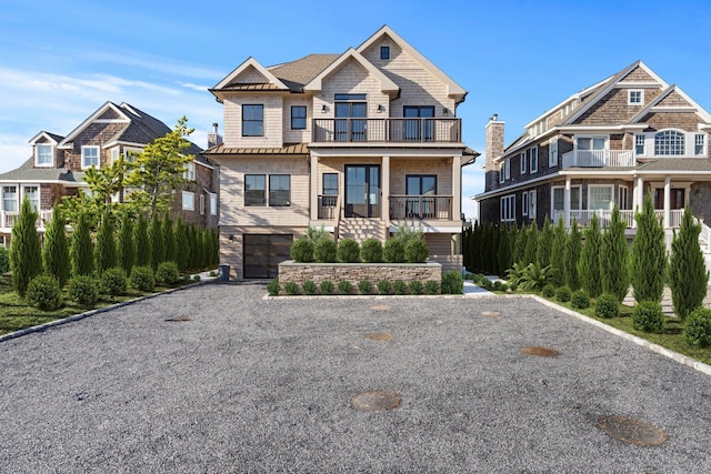 view of front of house featuring gravel driveway, a standing seam roof, metal roof, a balcony, and a garage