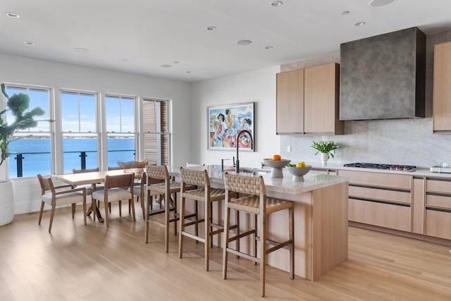 kitchen featuring backsplash, a sink, wall chimney range hood, and light wood finished floors